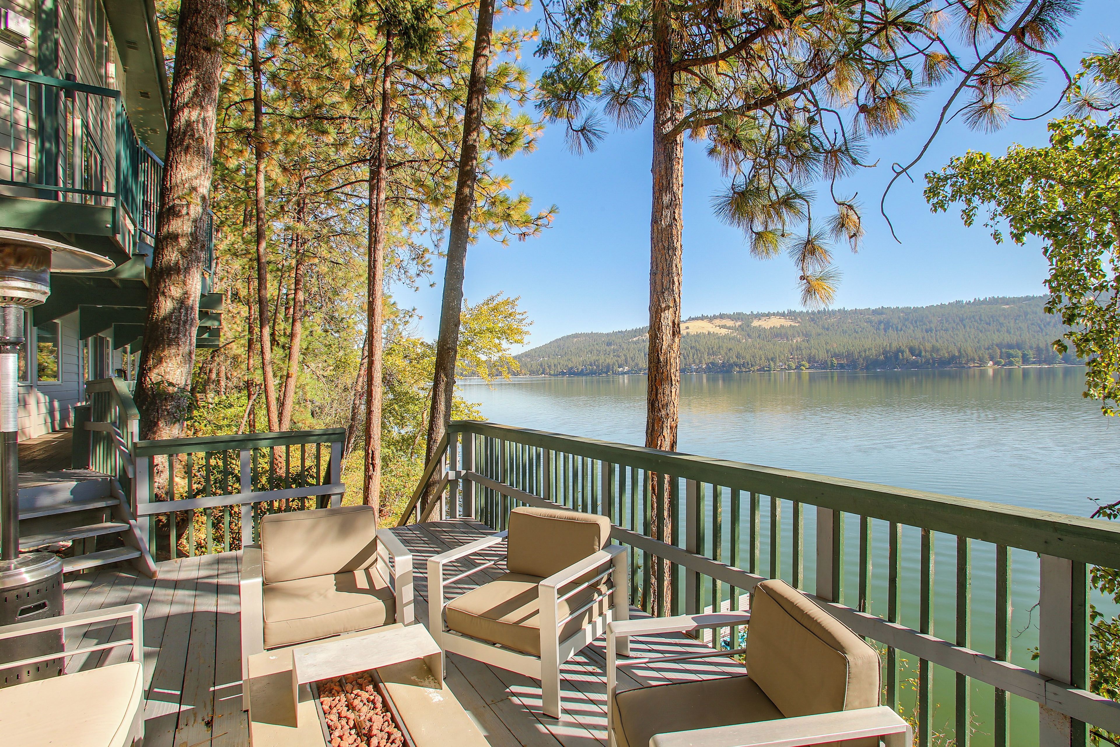 A deck with outdoor furniture overlooking a lake, surrounded by tall trees.