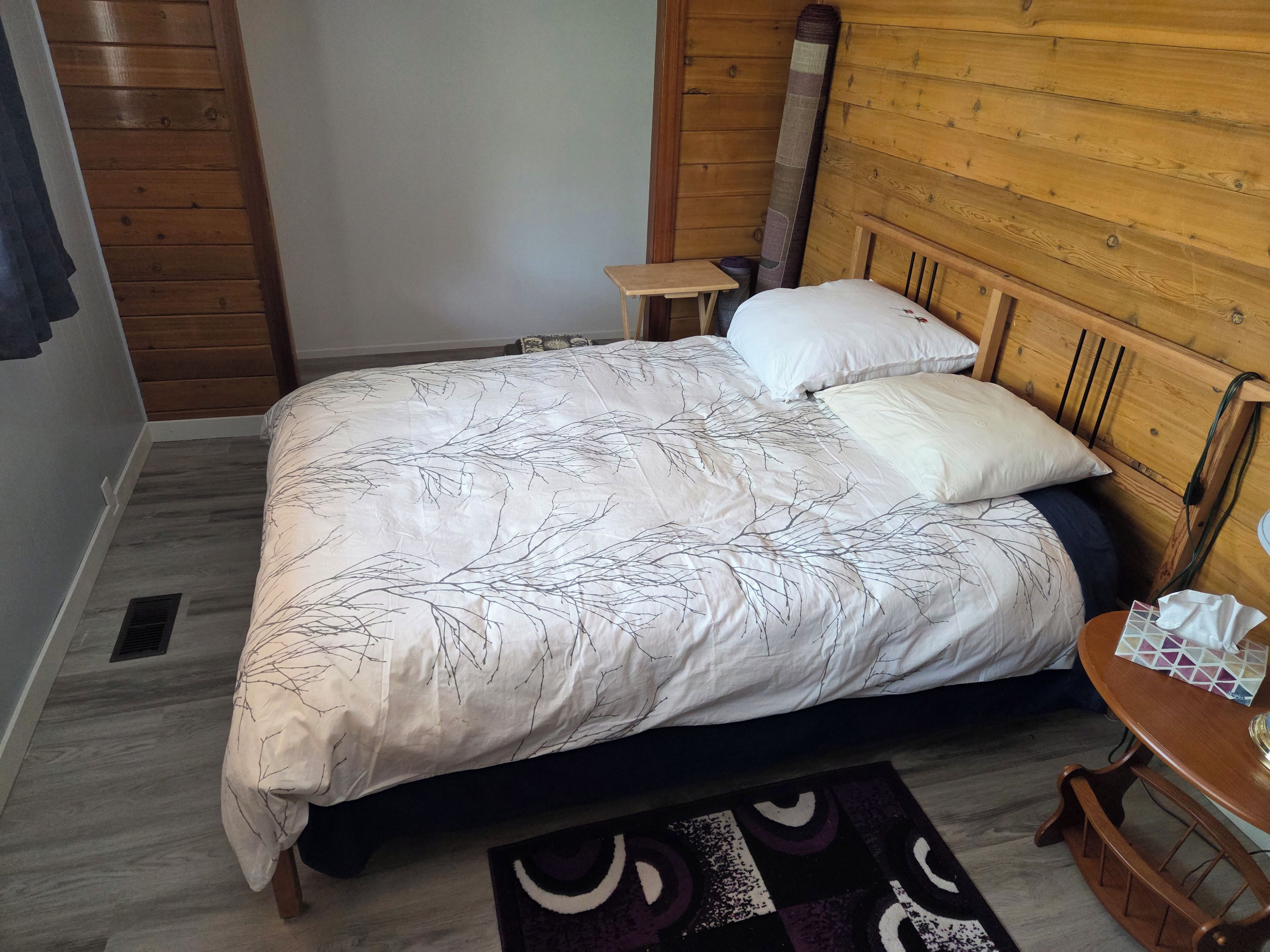 A bedroom with a bed, a nightstand, a wooden headboard, and a small table with a tissue box.