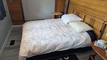 A bedroom with a bed, a nightstand, a wooden headboard, and a small table with a tissue box.