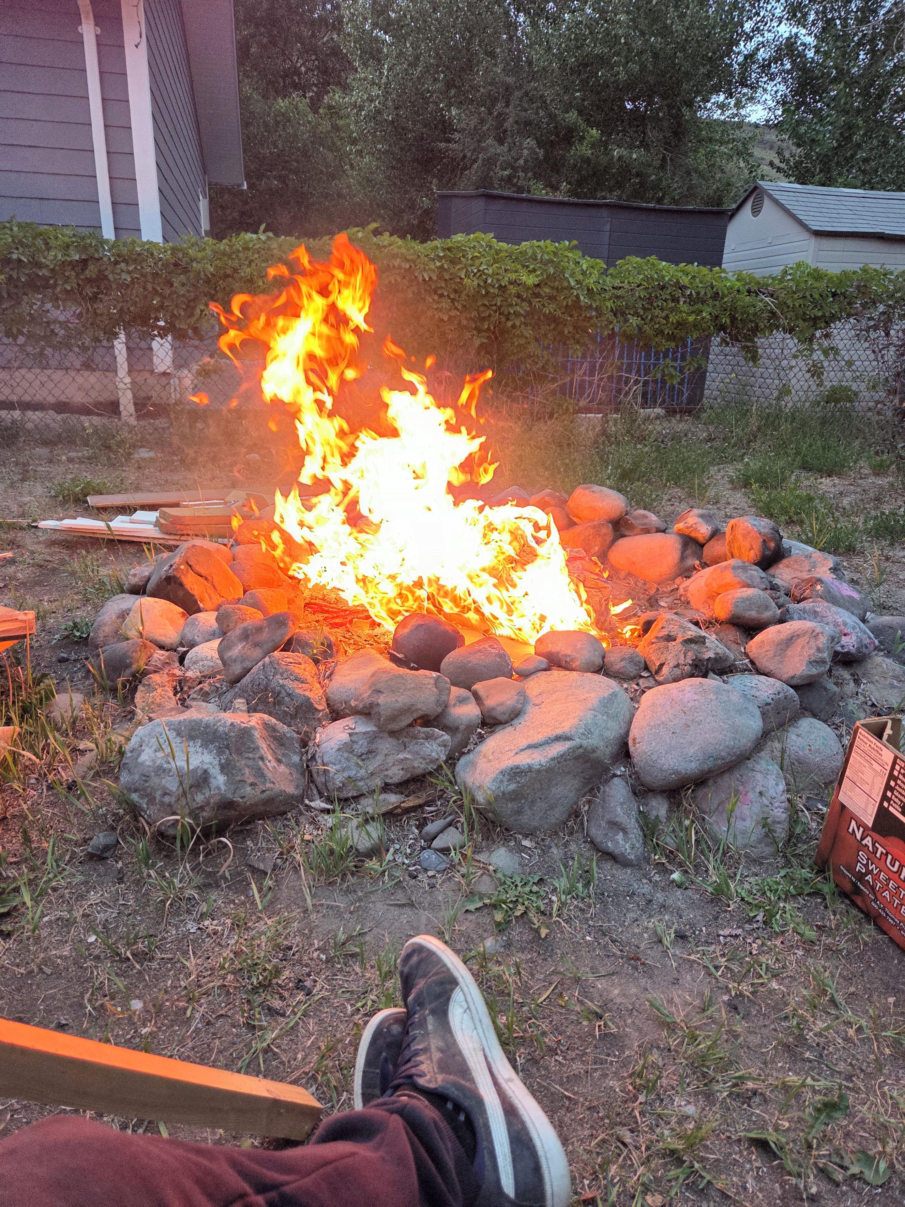 A campfire surrounded by rocks with a person's legs visible in the foreground.