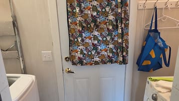 Une buanderie équipée d’un lave-linge, d’un sèche-linge, d’un rideau à motifs, d’un sac suspendu et d’un petit tapis.