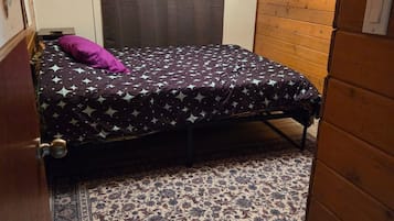 Una habitación pequeña con cama individual, colcha estampada, almohada morada y alfombra decorativa.