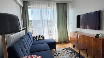 A modern living room with a blue sofa, a wooden cabinet, a television, and a patterned rug.