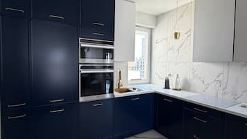 A modern kitchen with dark cabinetry, stainless steel appliances, and a marble backsplash.