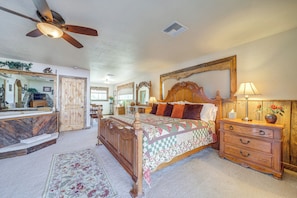 A bedroom with a wooden bed, a nightstand, a dresser, a ceiling fan, and a large mirror.