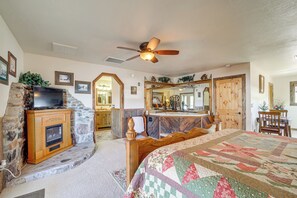 A bedroom with a stone fireplace, a television, a ceiling fan, and a large bed with a quilt. - Romantic Mtn-view Suite w/ Jacuzzi Tub in Pine (Pine)