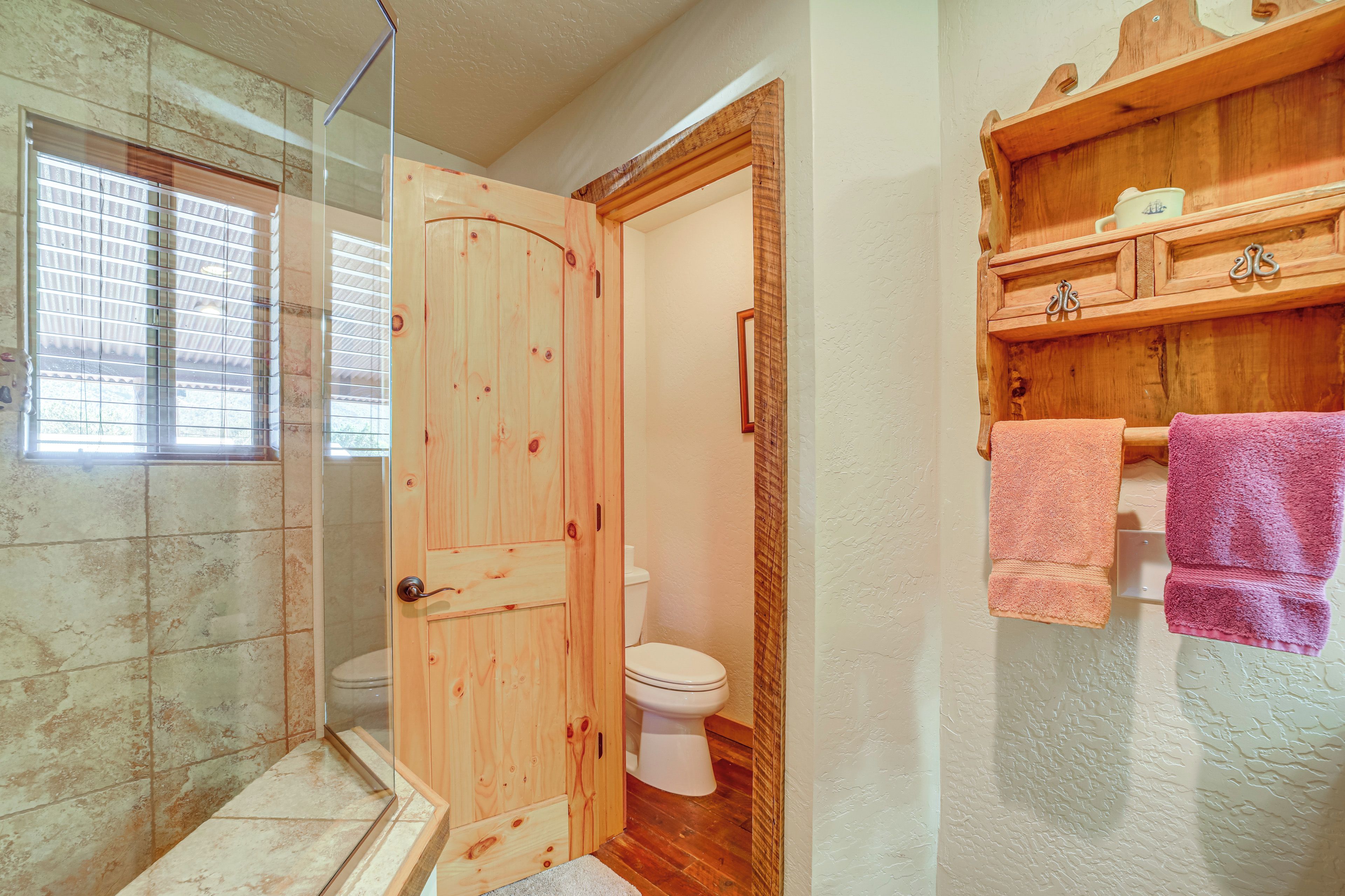 A bathroom with a wooden door, a toilet, a shower area, and a wooden shelf with towels.