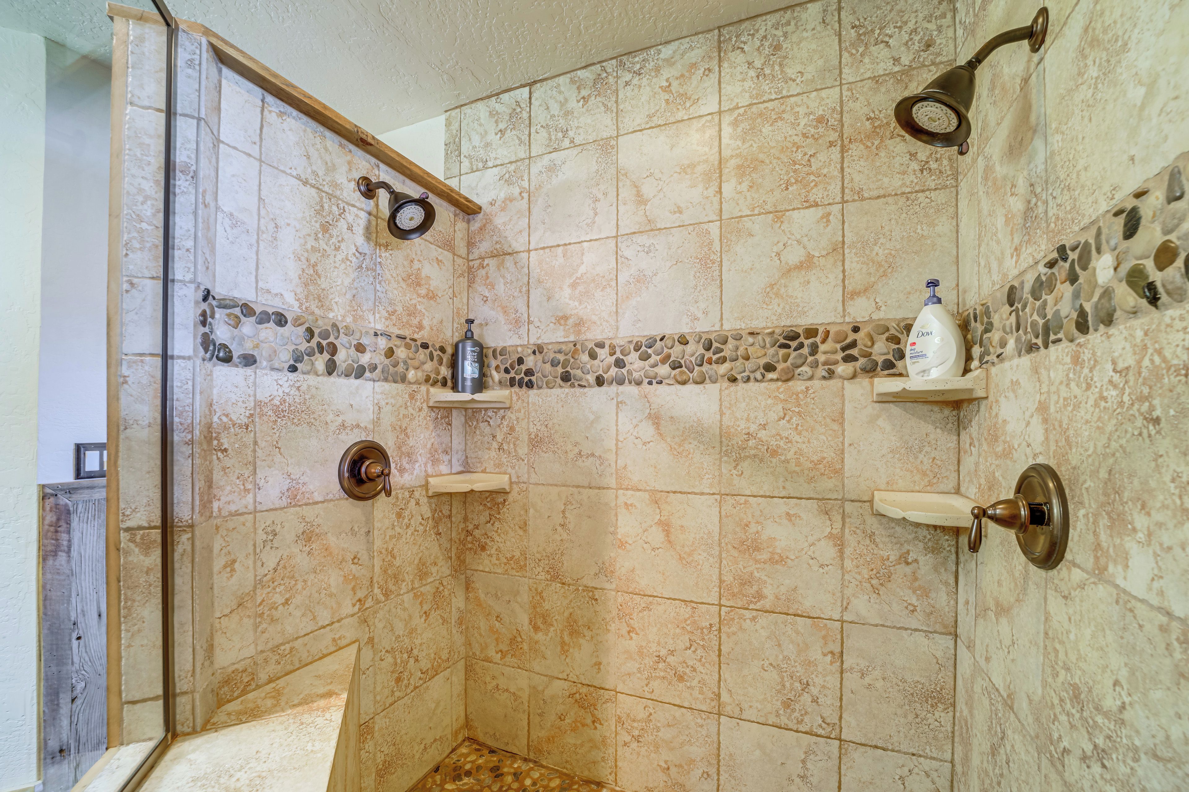 A shower with a glass door, a handheld showerhead, and a bottle of Dove body wash on a shelf.