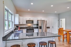 A modern kitchen with white cabinets, stainless steel appliances, a granite countertop, and a bar stool seating area. - Large Deck w/ Views! Brand New Three Rivers Home (Three Rivers)