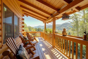 A wooden deck with a view of mountains, a bench, and a birdhouse.