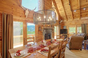 A wooden cabin interior with a dining area, a fireplace, and a television in the living room.