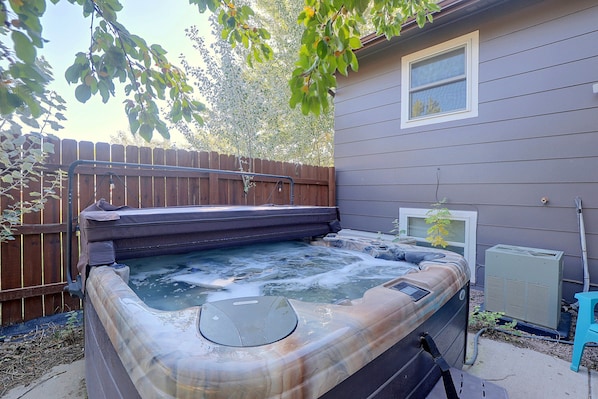 A hot tub in a backyard with a wooden fence and a house in the background.