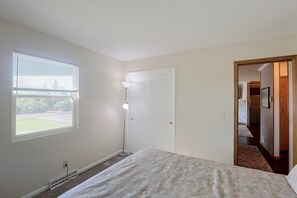 A bedroom with a bed, a window with blinds, a standing lamp, and a door leading to another room. - Private Hot Tub! Spacious Home in Rapid City (Rapid City)