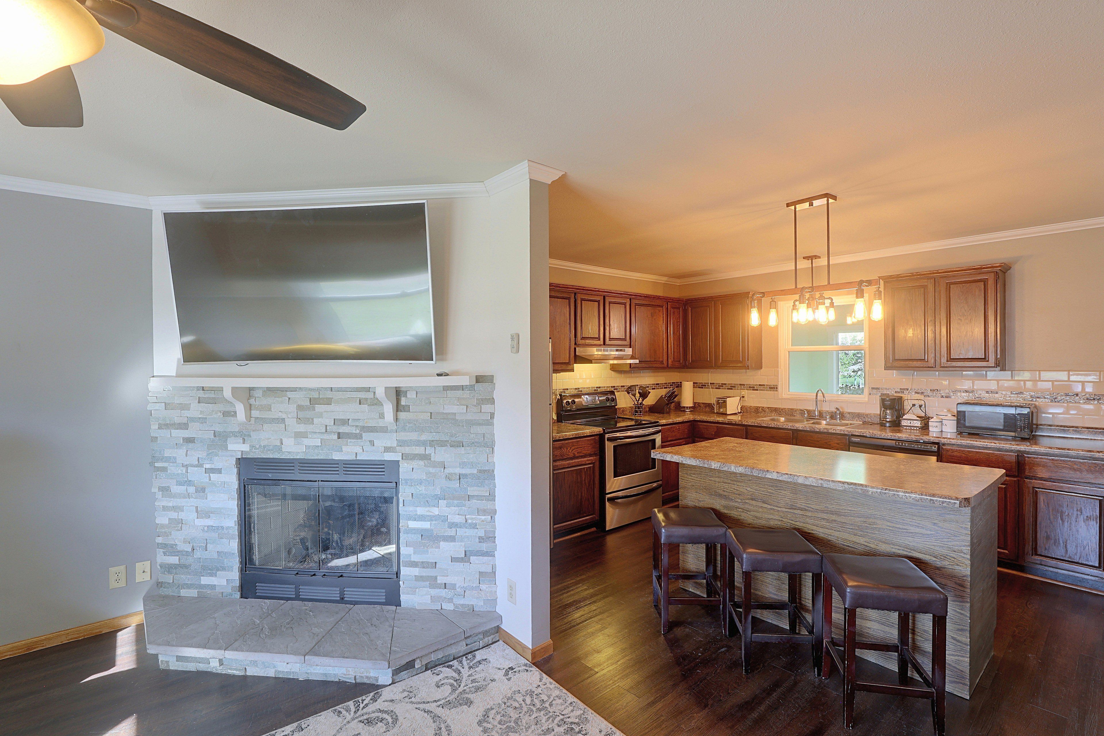 A modern kitchen with a stone fireplace, wooden cabinets, and a large island with bar stools.