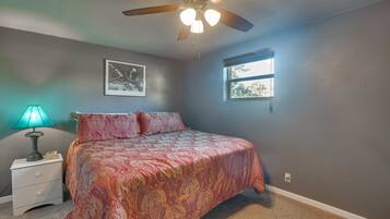A bedroom with a bed, a nightstand, a ceiling fan, a window, and a wall-mounted picture.
