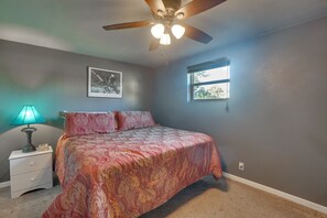 A bedroom with a bed, a nightstand, a ceiling fan, a window, and a wall-mounted picture.