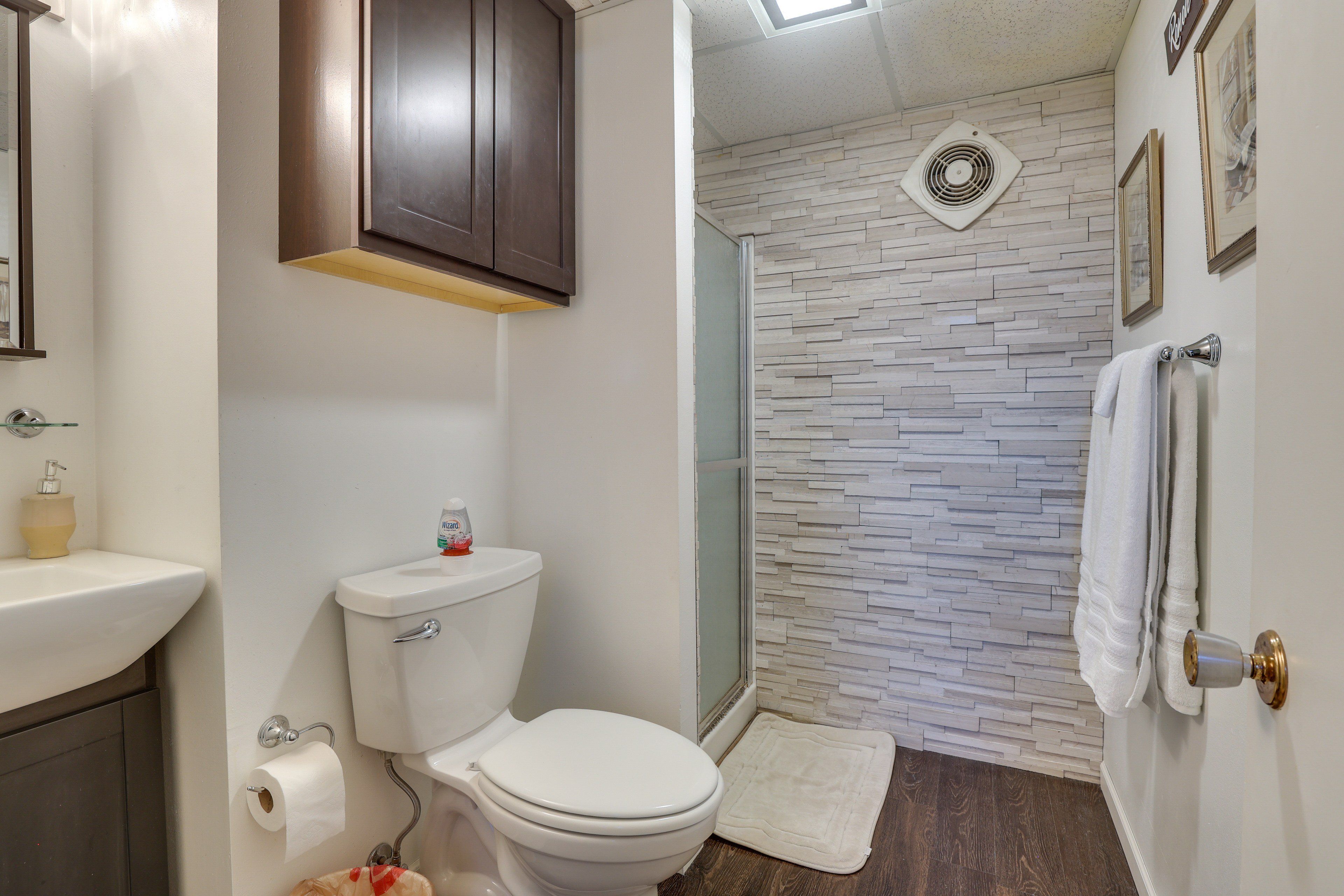 Un baño con inodoro, lavamanos y zona de ducha con pared de piedra.