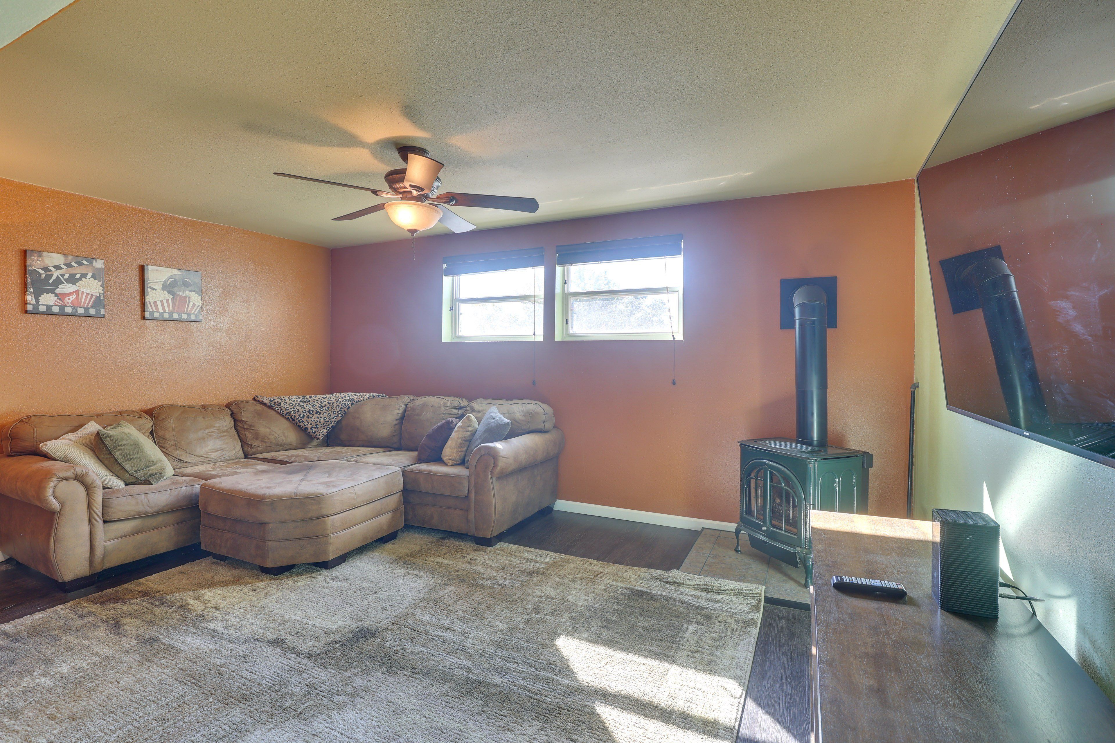 A living room with a sectional sofa, a ceiling fan, a fireplace, and two windows.