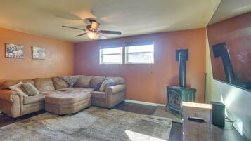 A living room with a sectional sofa, a ceiling fan, a fireplace, and two windows.