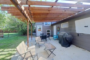 A covered patio area with outdoor furniture, a grill, and a house in the background.