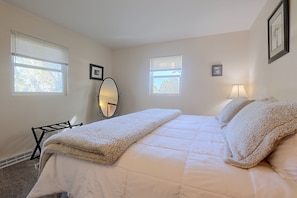 A bedroom with a bed, two windows, a mirror, and a lamp.