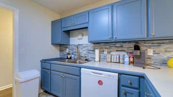A kitchen with blue cabinets, a dishwasher, a sink, and a tiled backsplash.