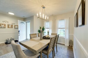 A dining room with a wooden table, chairs, a chandelier, and a view of the outdoors through the windows.