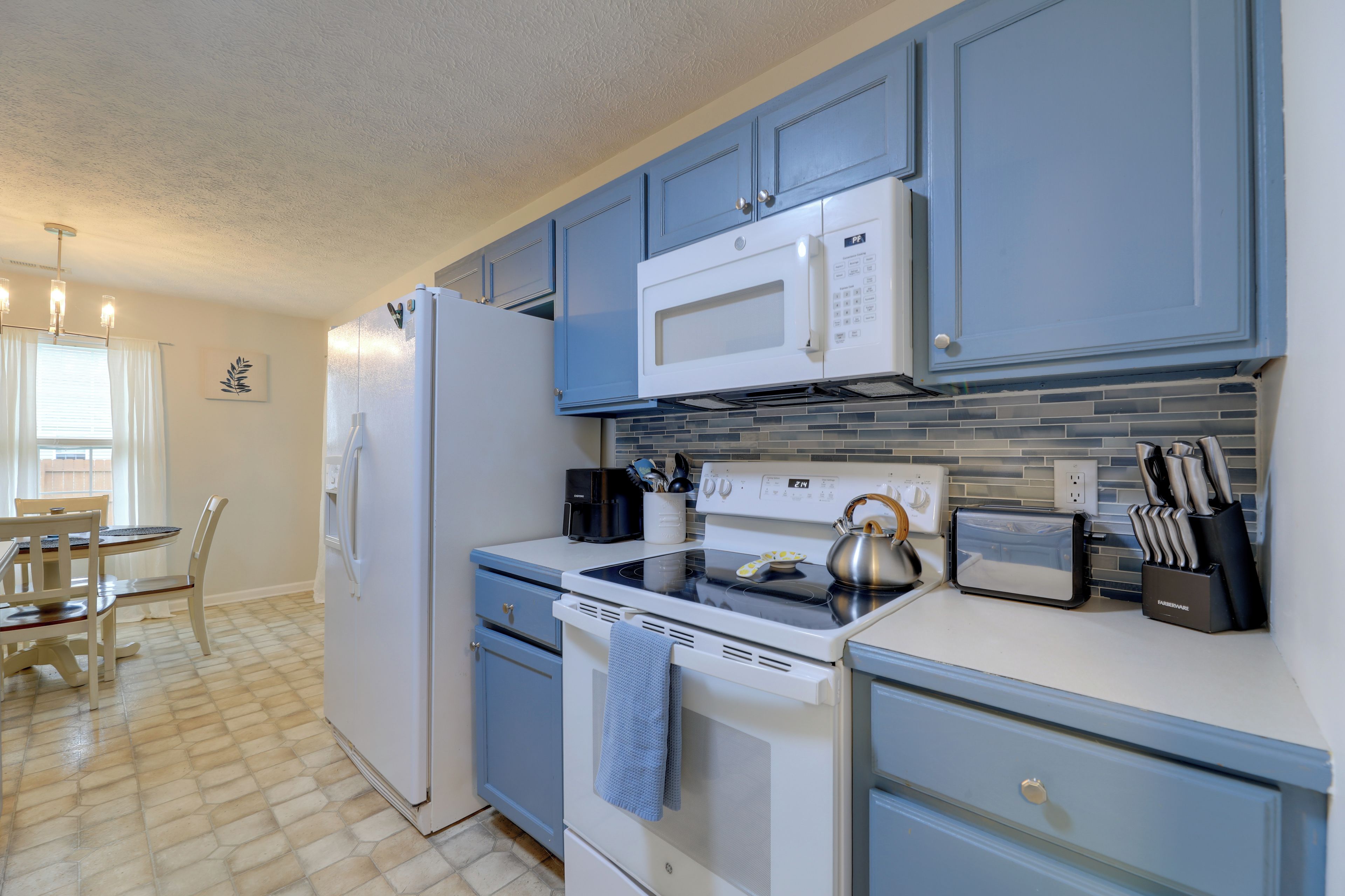 Cocina moderna con refrigerador, microondas, estufa y horno. Cuenta con un comedor con mesa y sillas.