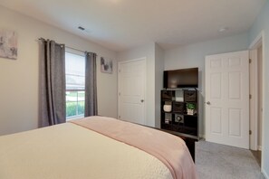 Un dormitorio con cama, cómoda, televisor y ventana con cortinas.