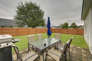 Un patio exterior con una mesa y sillas de vidrio, una parrilla y una sombrilla azul.