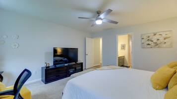 A bedroom with a bed, a television, a ceiling fan, and a door leading to another room.
