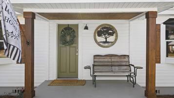 A white house with a green door, a bench, a wreath, and a welcome sign.