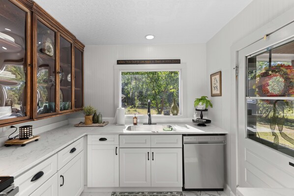 Una cocina moderna con armarios blancos, lavavajillas integrado y ventana con vistas a un jardín.