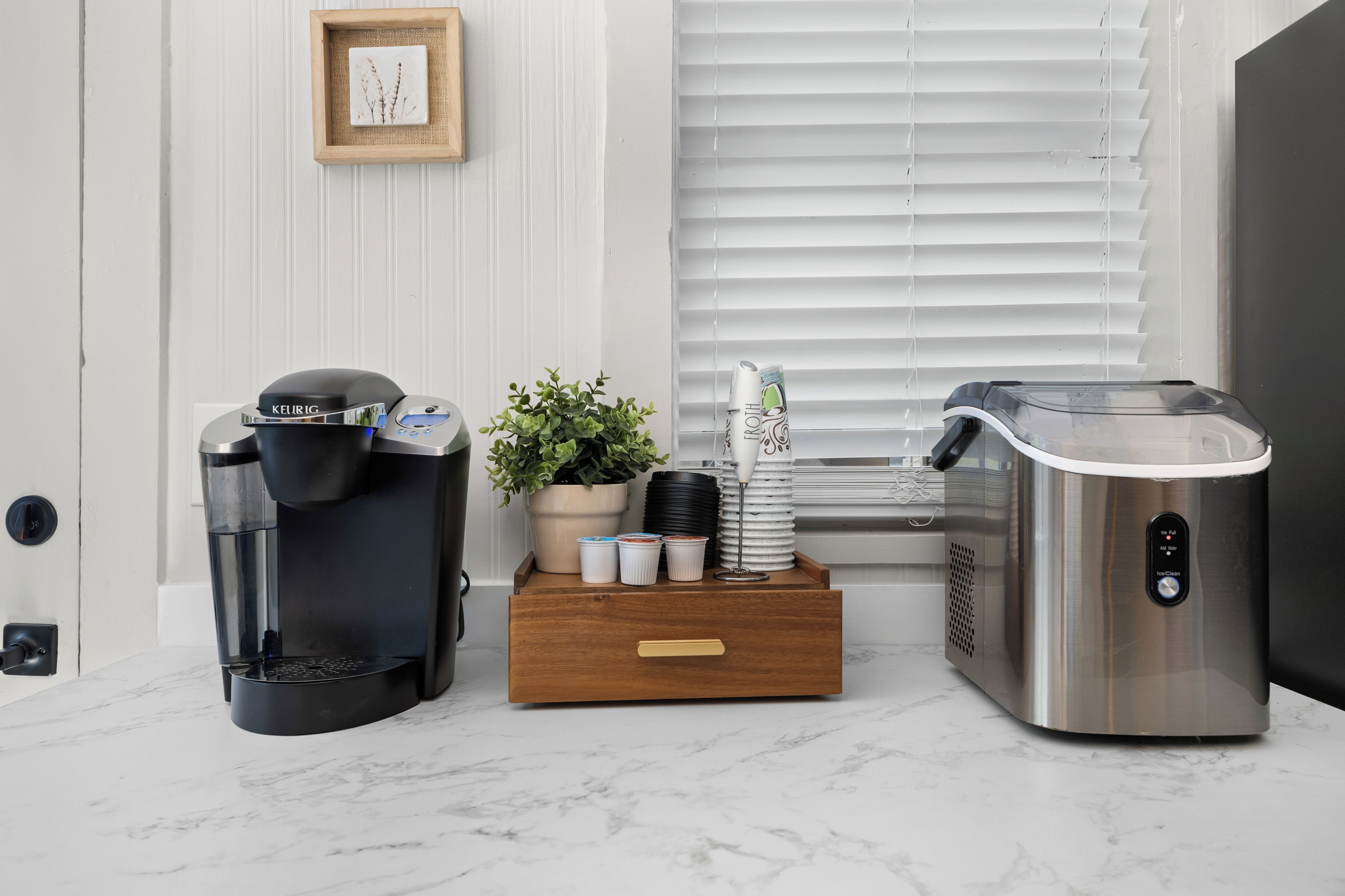 Una zona de cocina con cafetera, dispensador de agua y tetera sobre una encimera de mármol.