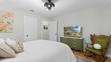 A bedroom with a bed, a television on a dresser, a rocking chair, and a painting on the wall.