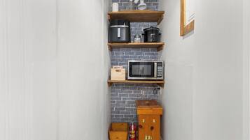 Une cuisine avec un mur en briques, des étagères en bois, un four à micro-ondes, une bouilloire et un extincteur.
