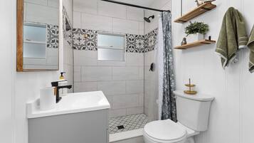 A bathroom with a shower, toilet, sink, and a mirror.