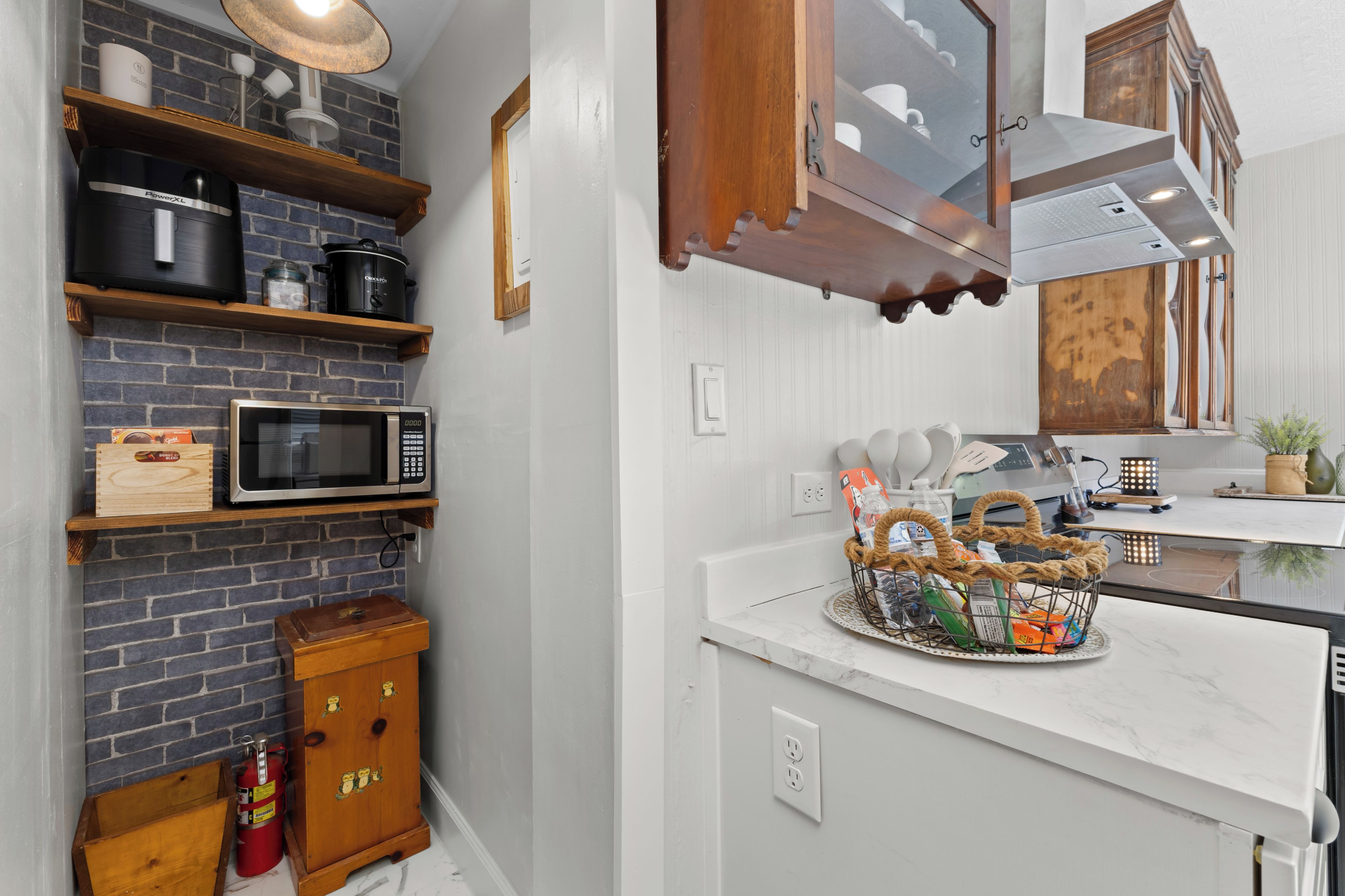 Una cocina con pared de ladrillo, estantes de madera, microondas, mueble de madera y encimera con una cesta.