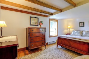 Un dormitorio con cómoda de madera, cama con colcha estampada, mesita de noche con lámpara y ventana con vista al exterior.