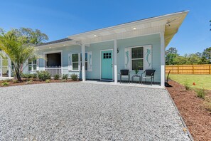 A light blue house with a covered porch, a gravel driveway, and a wooden fence in the background. - 2-unit Ocean Isle Beach Getaway Near Pier & Dining (Ocean Isle Beach)