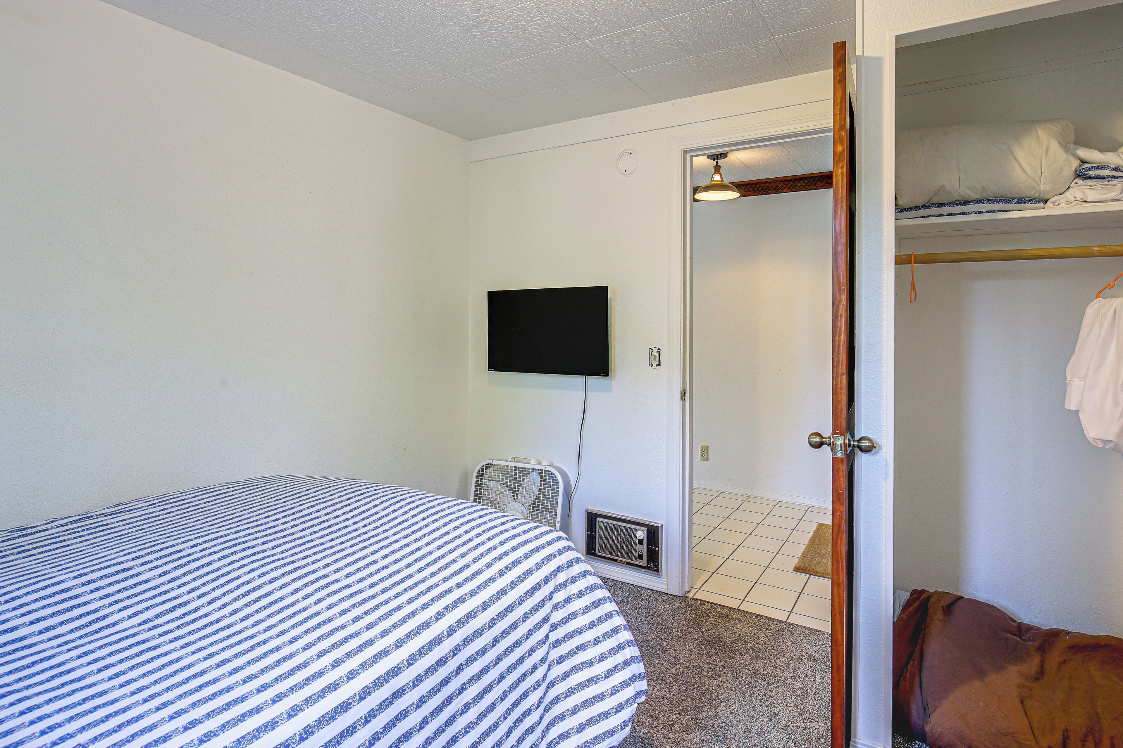 Una habitación con una cama, un televisor instalado en la pared y una puerta que da a un armario con una percha.