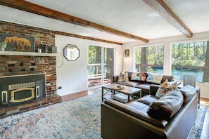 A living room with a fireplace, leather sofa, and large windows overlooking a body of water.