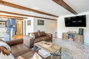 A living room with a brown leather sofa, a wooden coffee table, a flat-screen TV, and a cabinet with a speaker. - Mckenzie River Home w/ Waterfront Fire Pit (Vida)