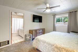 A bedroom with a bed, a ceiling fan, a TV, a radiator, and a window with curtains.