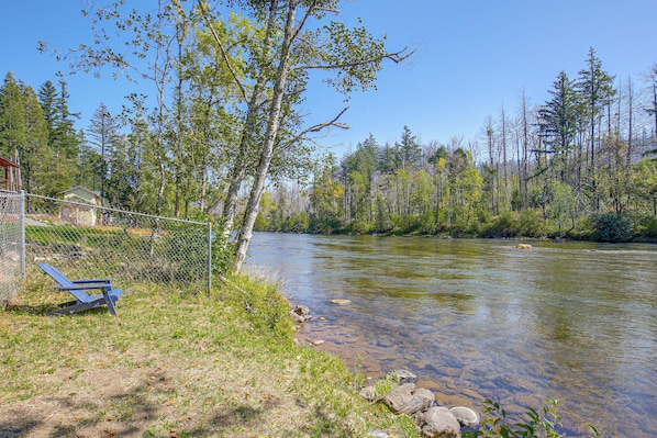 A river with clear water, surrounded by trees and a fence.