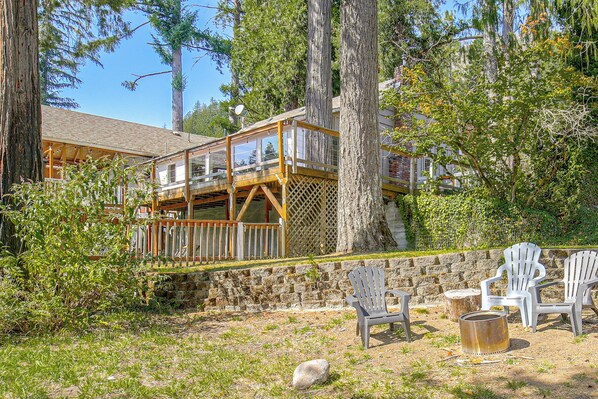 A cabin with a deck, surrounded by trees and a stone wall.