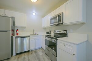 Una cocina compacta con gabinetes blancos, lavavajillas de acero inoxidable, microondas y horno.