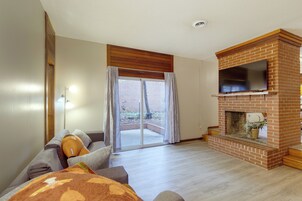 Una sala de estar con chimenea de ladrillo, un sofá, un televisor y una puerta corrediza de vidrio que da a un patio.