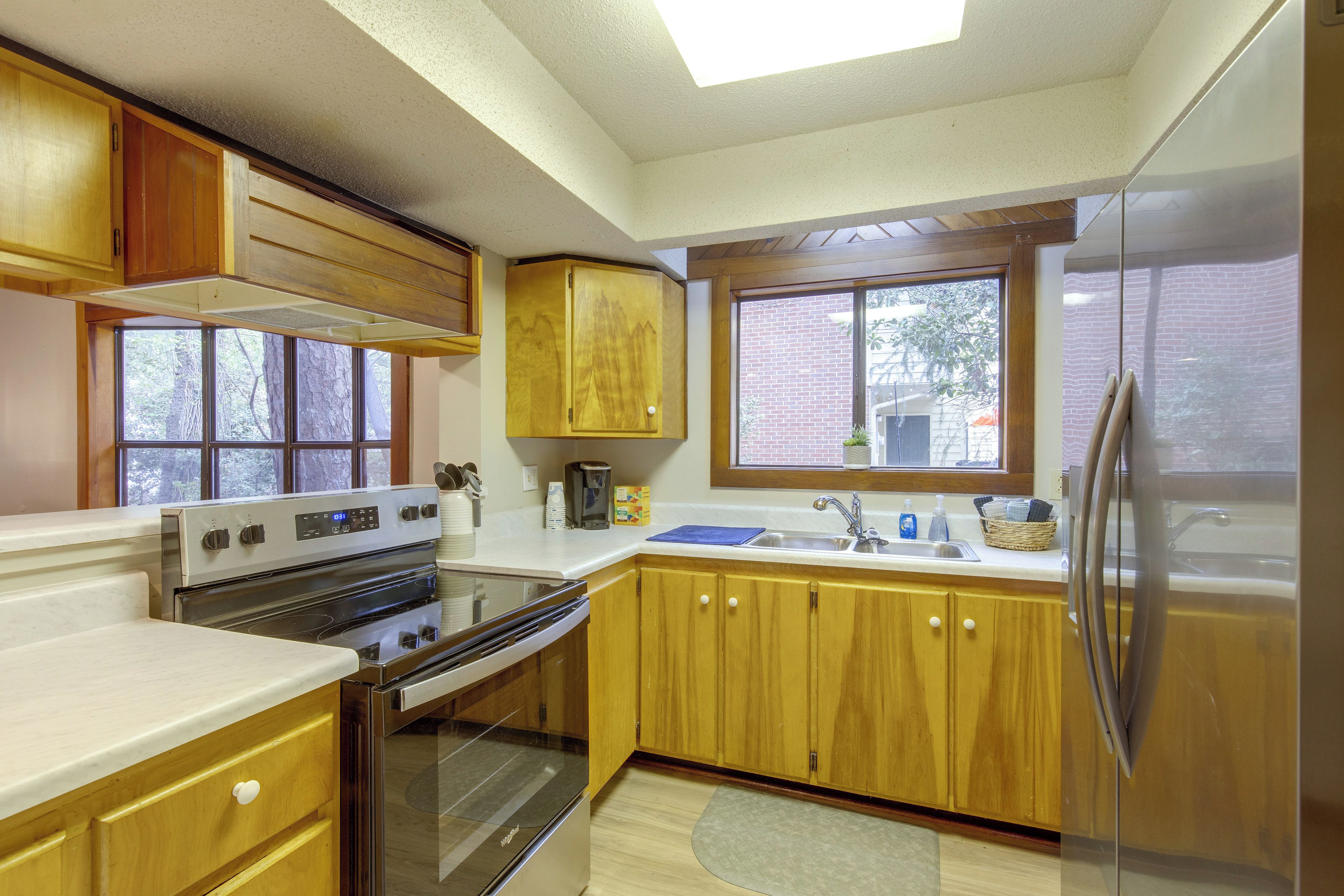 A kitchen with wooden cabinets, a stainless steel refrigerator, a built-in oven, and a window with a view of a brick wall and trees.
