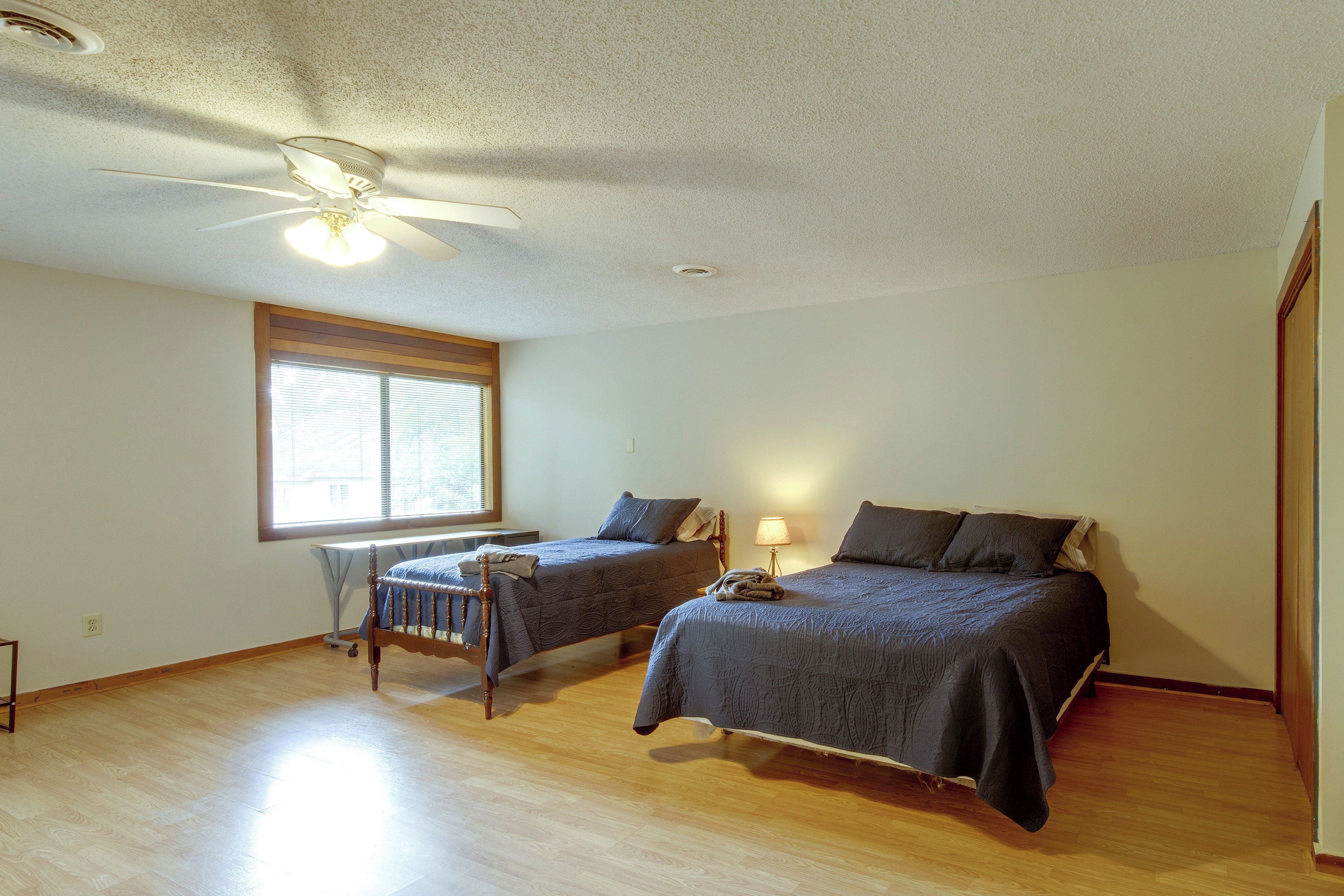 A bedroom with two beds, a ceiling fan, a window with blinds, and a bedside lamp.